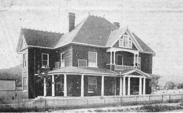 A two-story Victorian house with a wraparound porch and fenced yard.