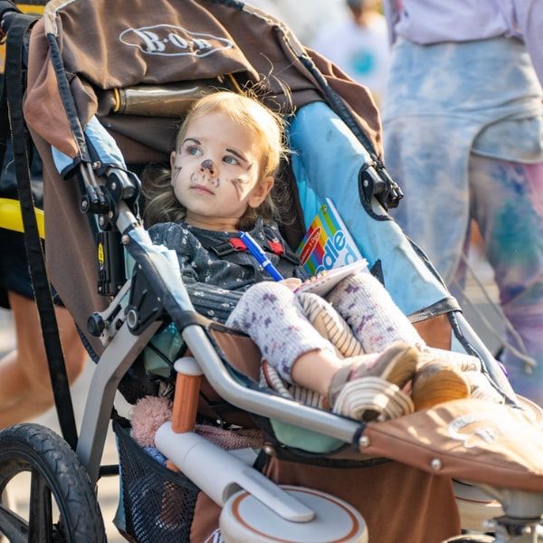 Child in a stroller with face paint, looking forward at an outdoor event.