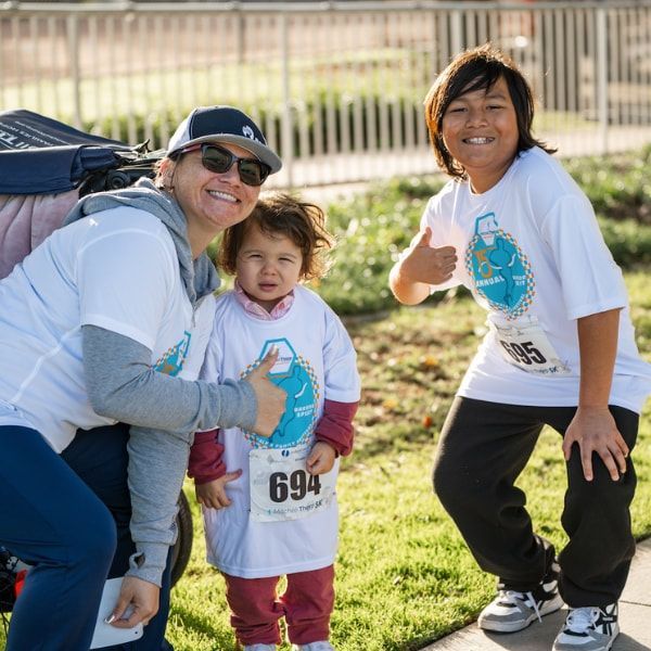 Three people smiling at a fun run, wearing matching shirts, one giving a thumbs-up.