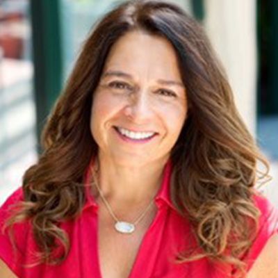 Woman with long brown hair, smiling, wearing a red shirt and a necklace.
