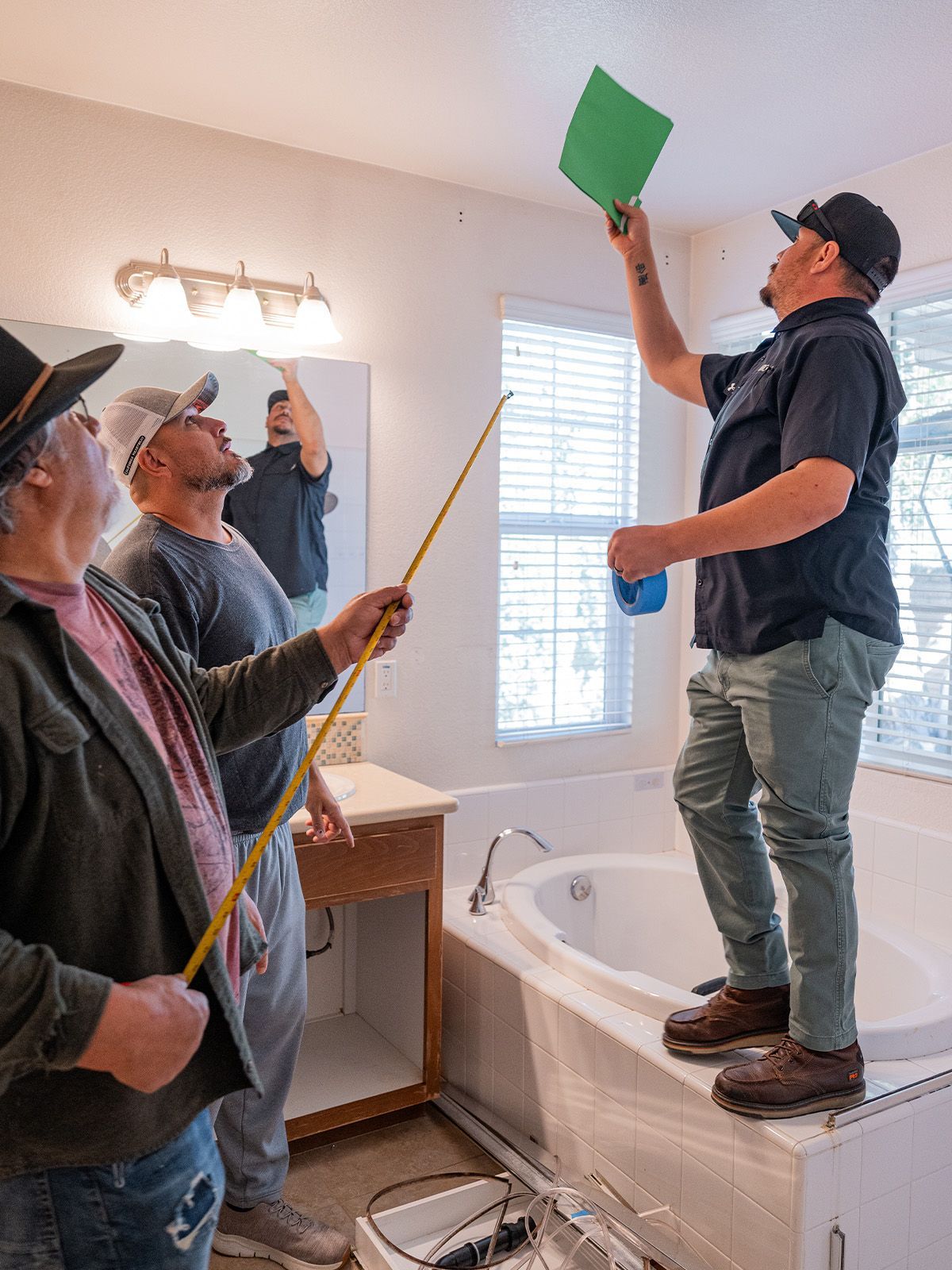 Four people inspecting a bathroom. One stands on the tub, holding a green paper, others use a measuring stick.
