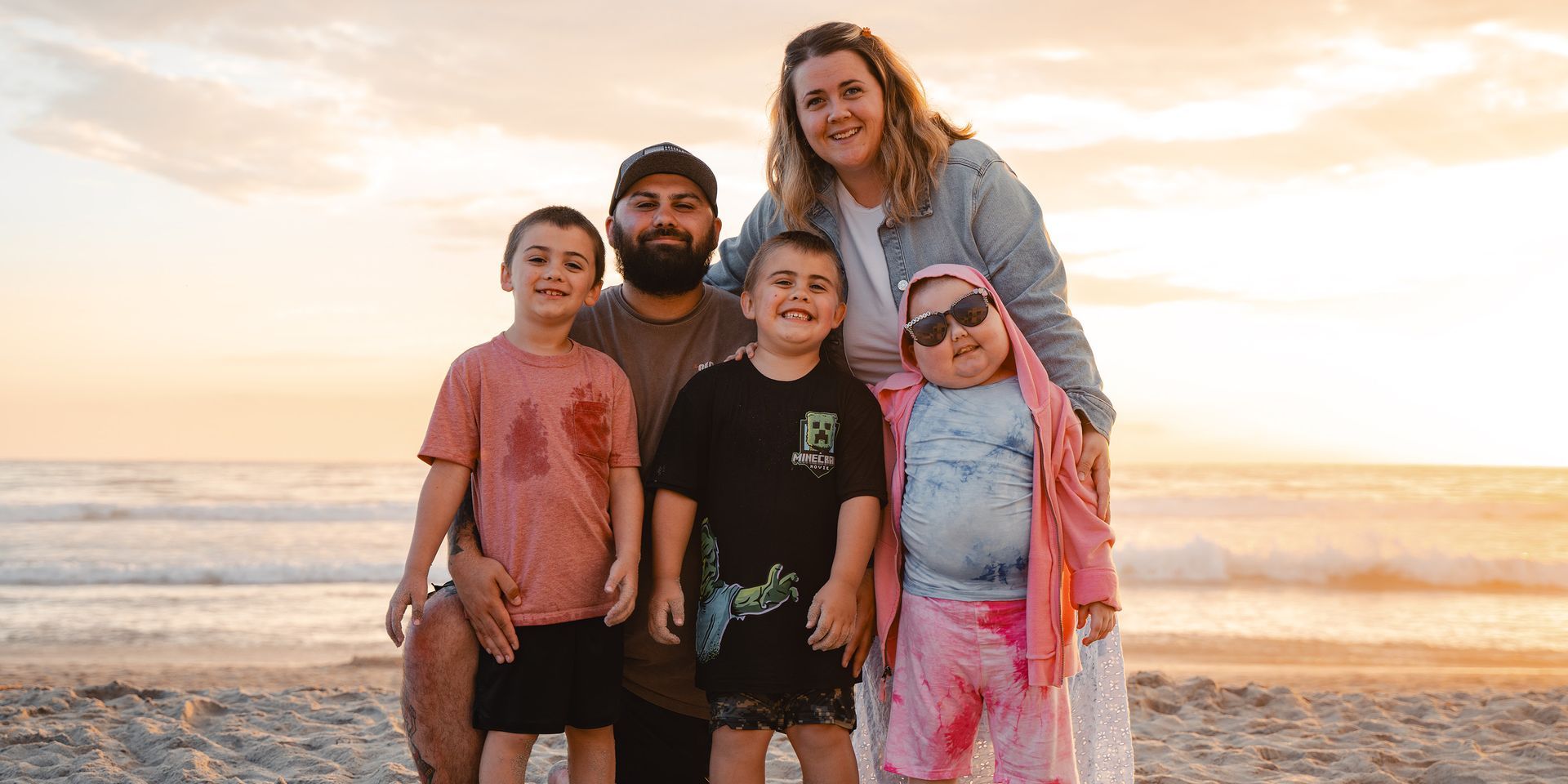 Family of five smiling at beach during sunset.