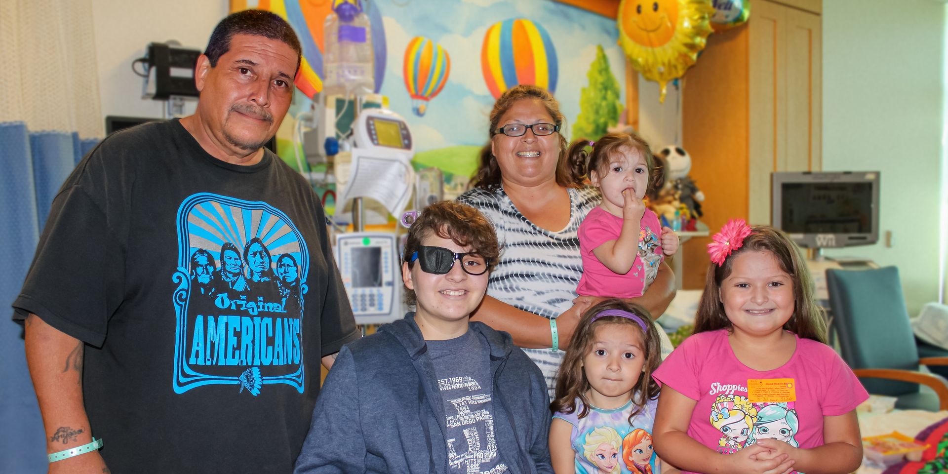 A family poses in a hospital room. The group includes two adults and four children. Hot air balloon mural.