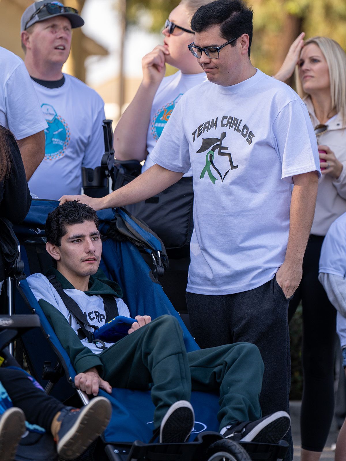 A young man in a wheelchair with supporters wearing