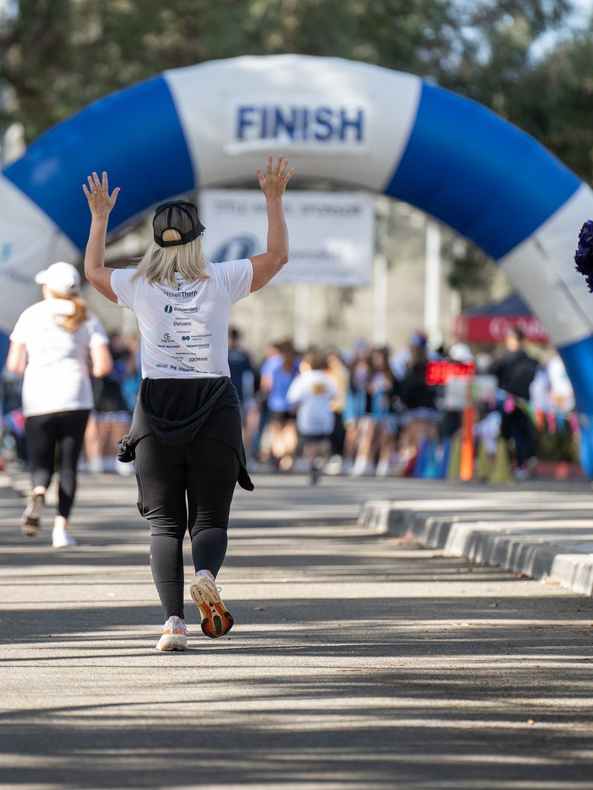 Woman running towards finish line, arms raised, celebrating completion of a race. Blue and white arch in background.