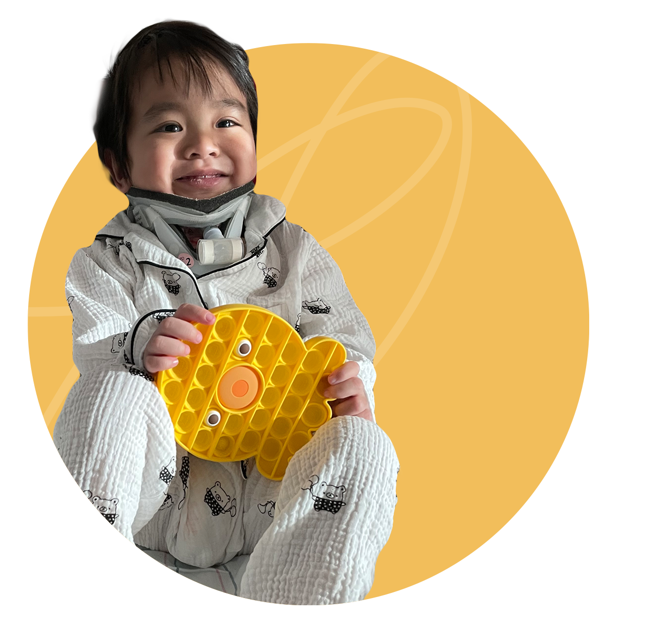Smiling toddler holding a yellow pop-it toy, wearing pajamas, sitting in front of a yellow circle background.