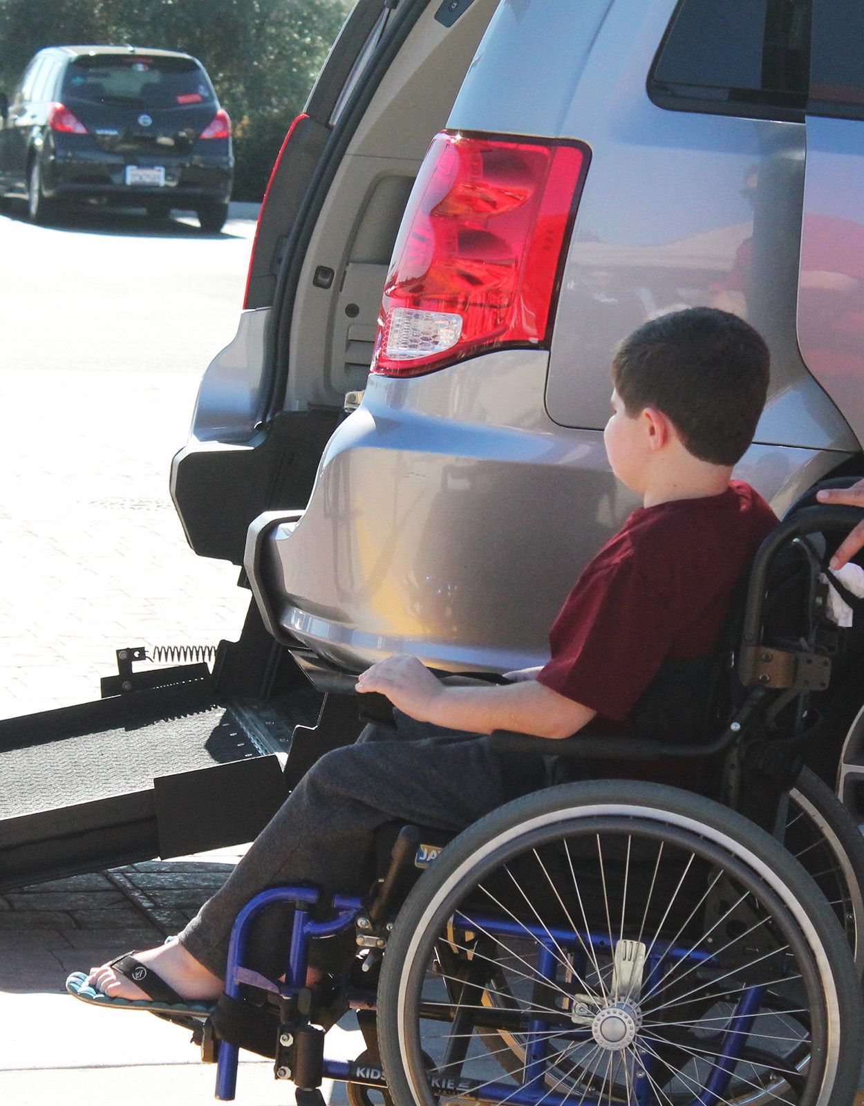 Boy in wheelchair near accessible van, ramp extended.