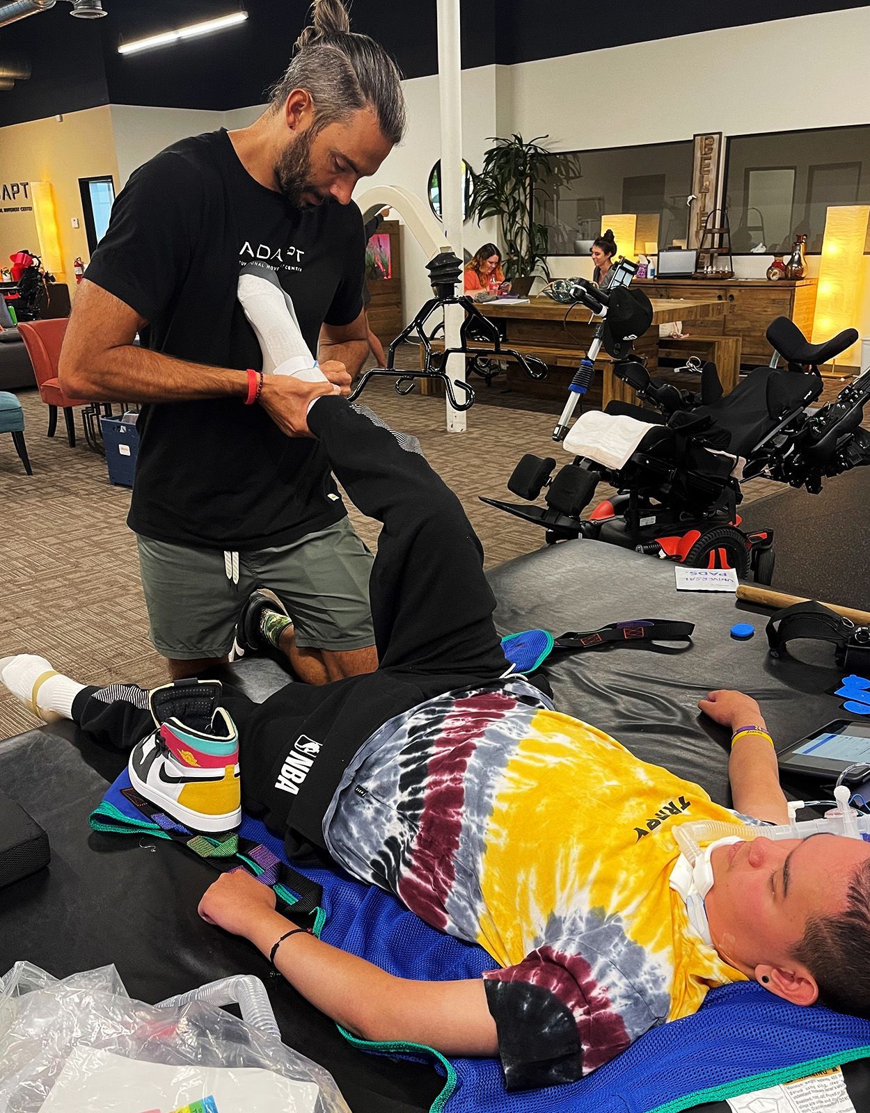 Man stretches the leg of a person lying on a table. Setting appears to be an office.