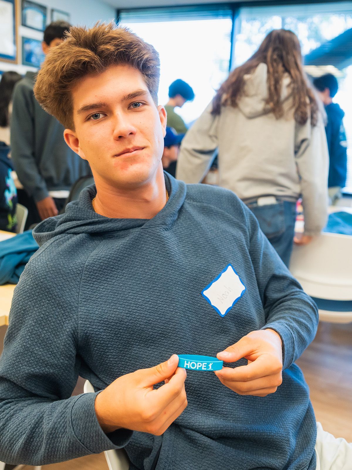 Man in blue hoodie holds name tag that says 