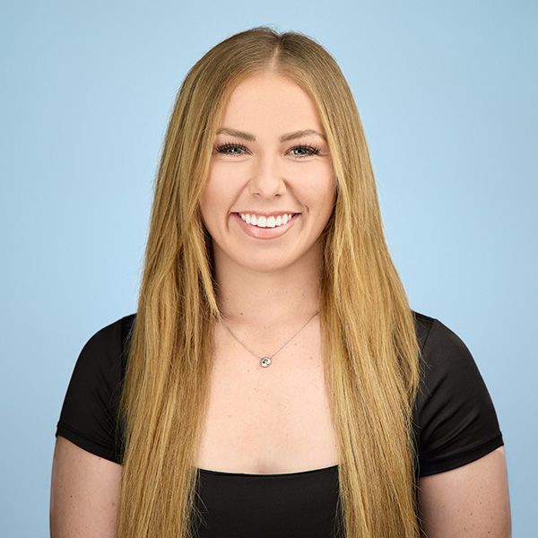 Woman with long brown hair, smiling, wearing a red shirt and a necklace.