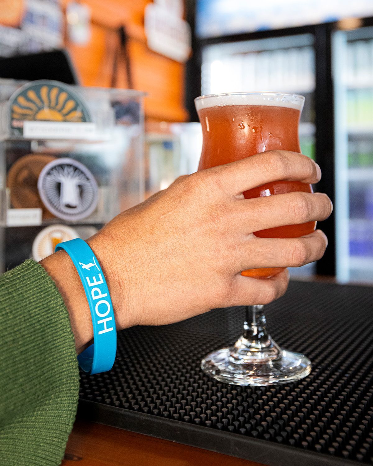Person holding a glass of amber beer, wearing a blue