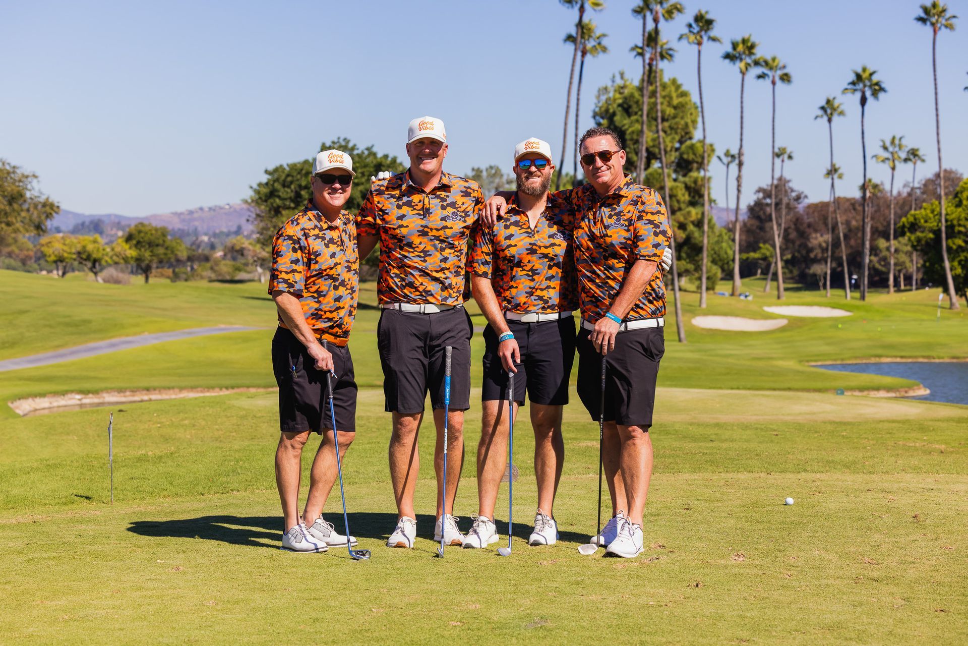 Four men in matching orange shirts and hats on a golf course posing for a photo.
