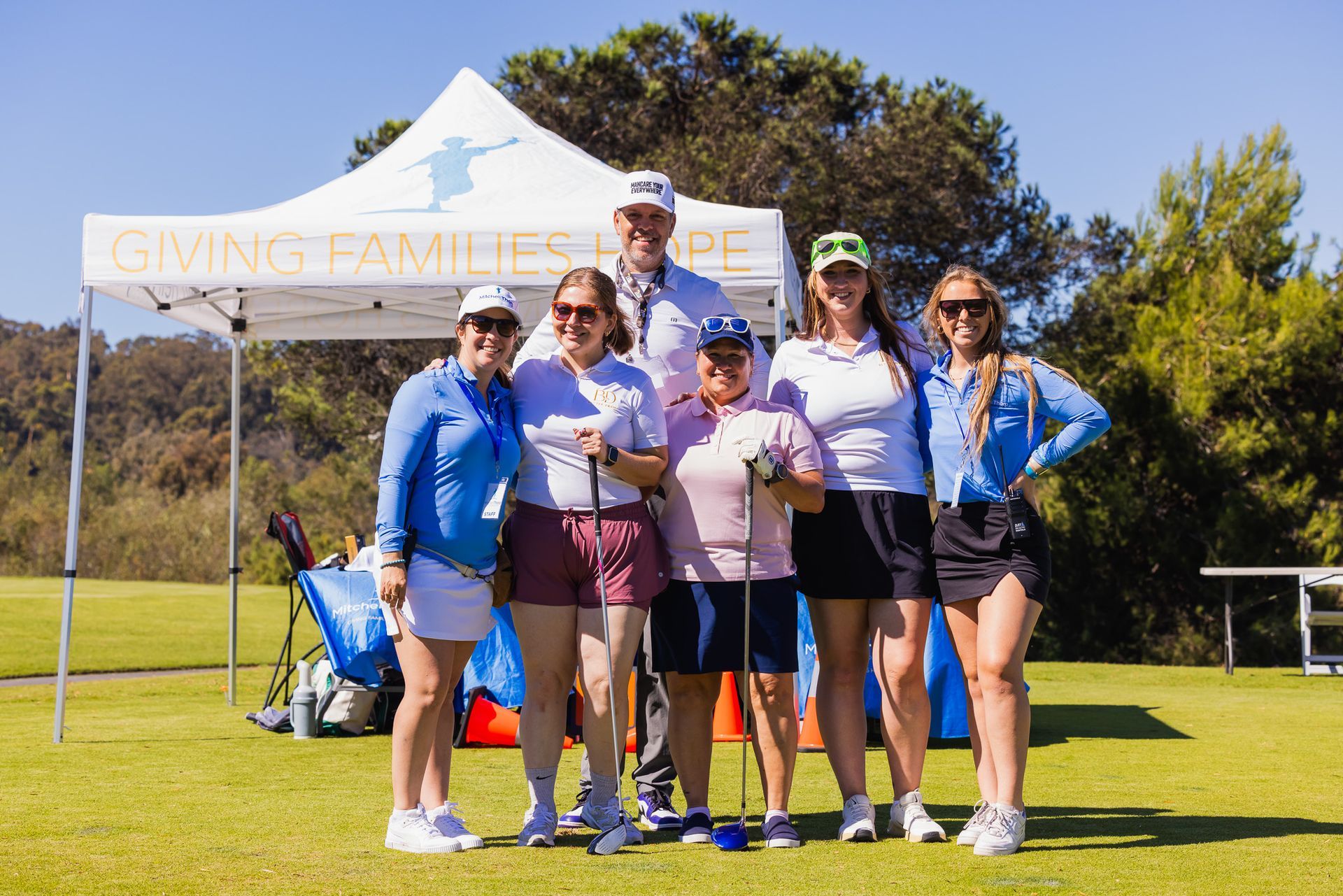 Group of people with golf clubs posing in front of a tent at a golf course.