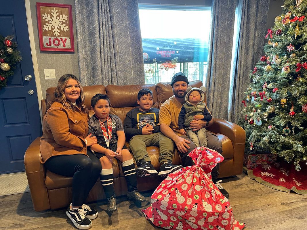 Family sitting on a sofa in front of a Christmas tree with presents; joyously looking towards the camera.