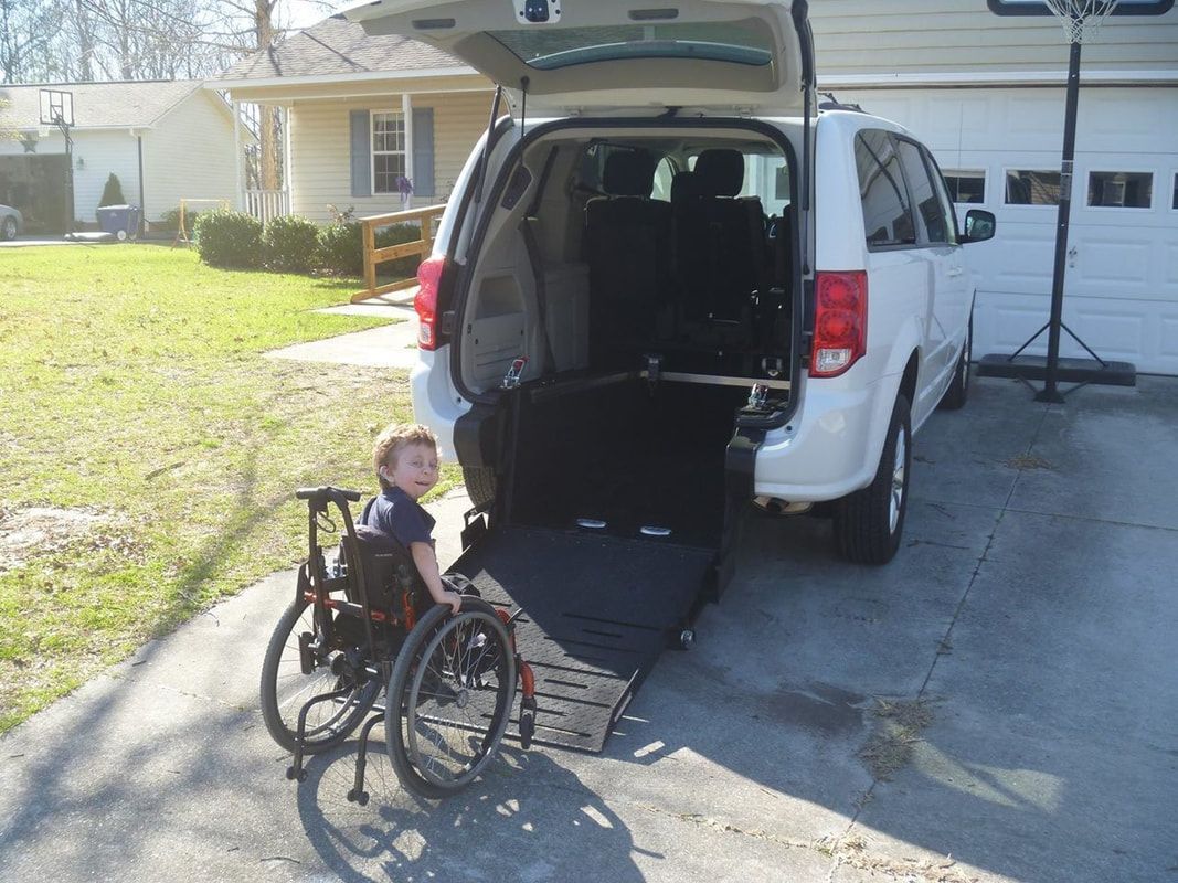 Child in wheelchair near a white van with lowered ramp. Home driveway.
