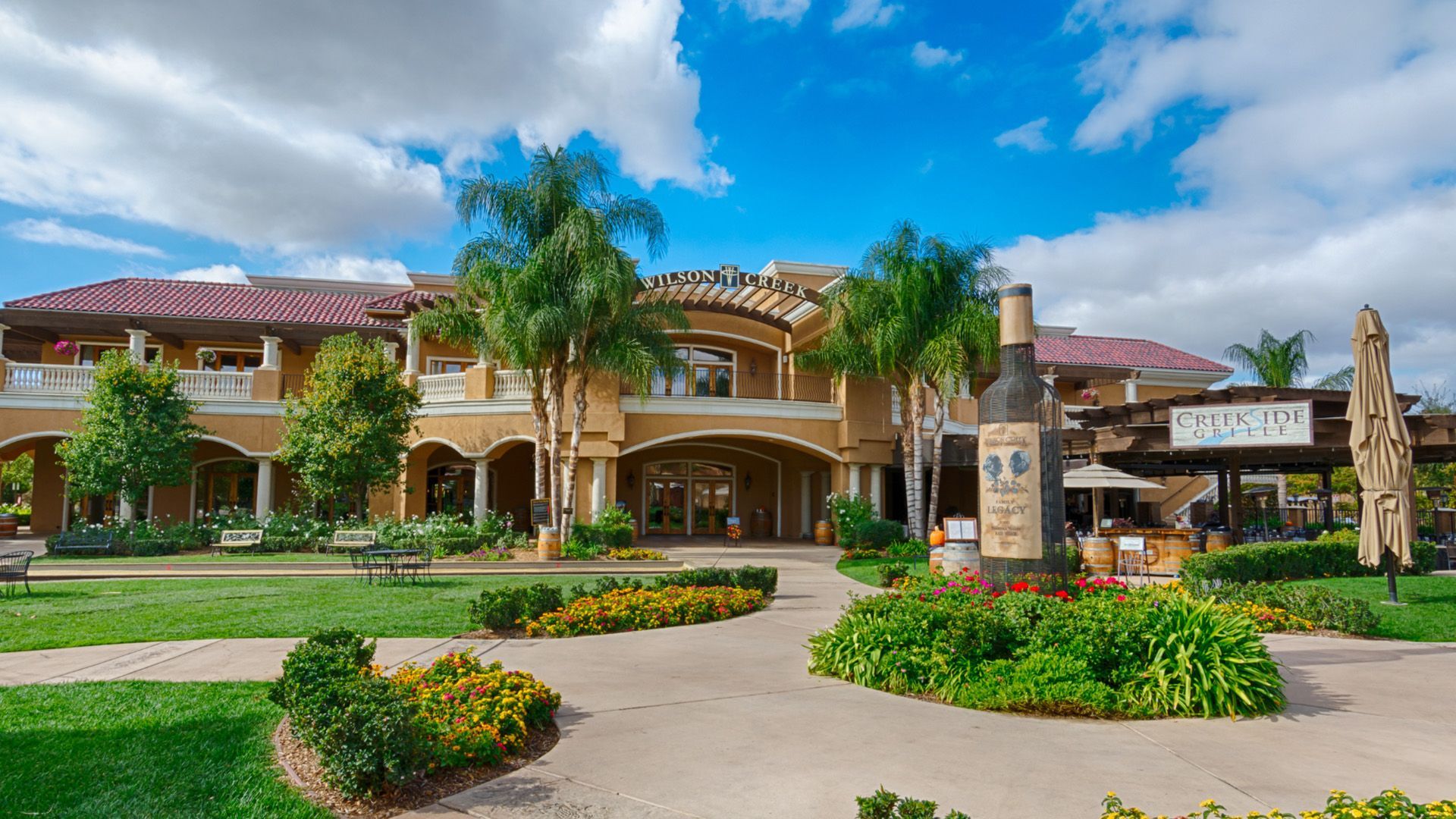 Exterior of a winery with a large bottle sculpture, lush landscaping, and a sunny sky.