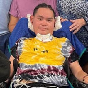 A person in a wheelchair wearing a tie-dye shirt, smiling.