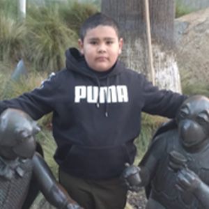 Boy in Puma hoodie, standing with arms out, flanked by turtle statues.