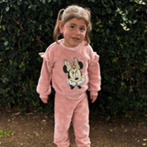 Young girl with pigtails in a pink Minnie Mouse outfit stands outside, smiling.