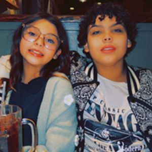 Two young people, girl in glasses, boy in patterned jacket, smiling, indoor setting.