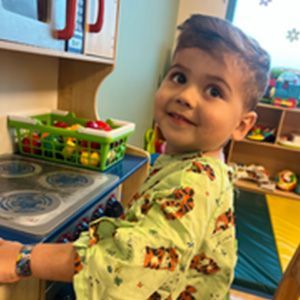 Boy in pajamas smiles while playing with a toy kitchen.