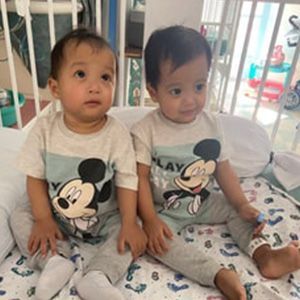 Two young children in matching Mickey Mouse shirts sit in a hospital bed.