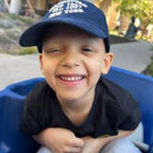 Smiling child wearing a blue baseball cap and black shirt, sitting in a blue container.