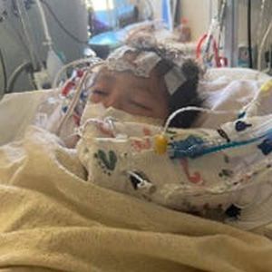 Newborn baby in a hospital bed with medical equipment attached; asleep with eyes closed.