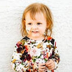 Young child with messy face, floral top, smiling, indoors.