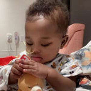 Young child with a nasal cannula in a hospital bed, holding a teddy bear.