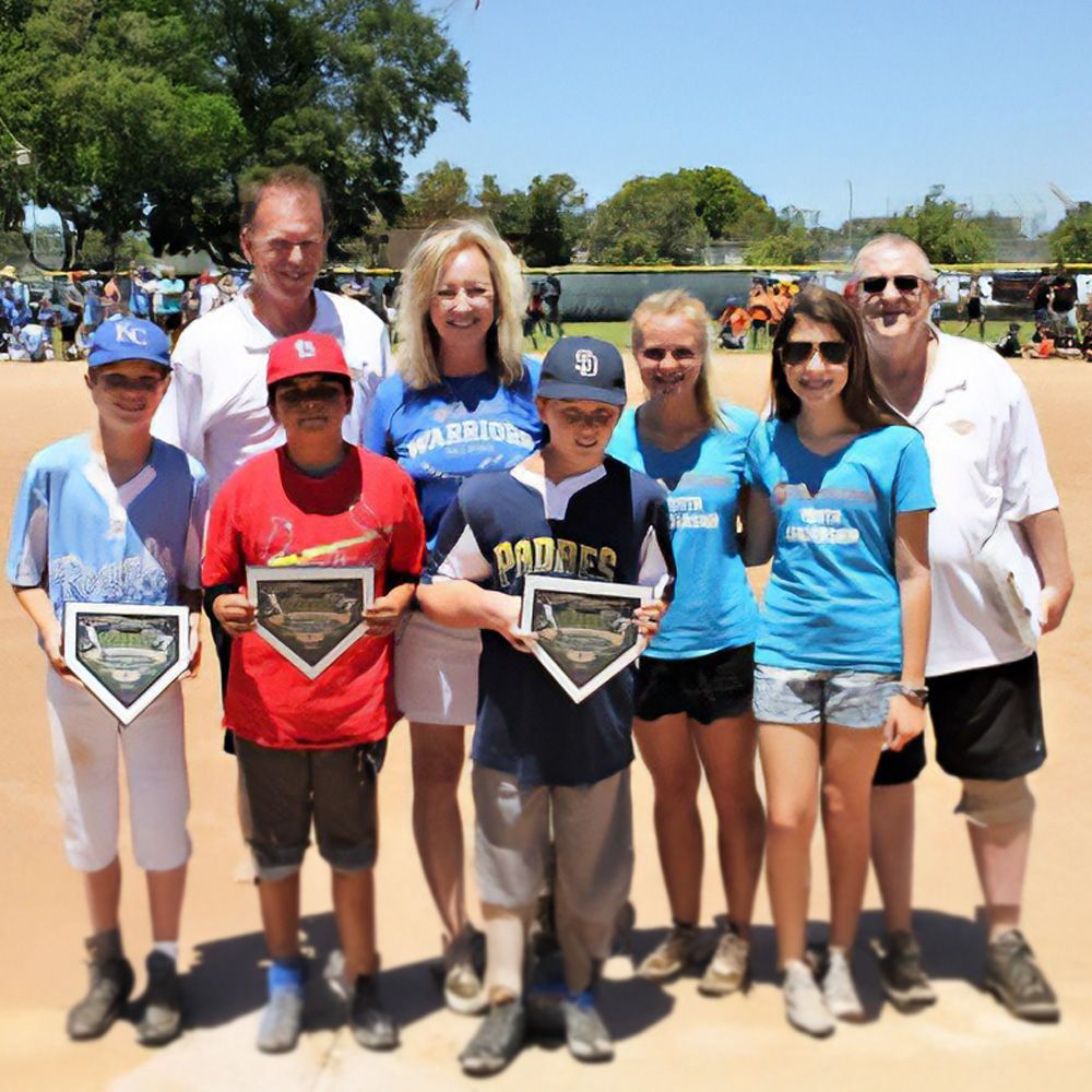 Group of people holding trophies on a baseball field on a sunny day.