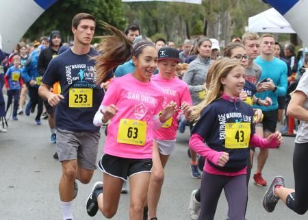People of various ages running a race, smiling, under an archway.