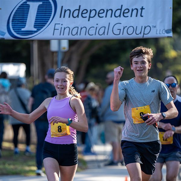Two runners with bibs near banner for Independent Financial Group.