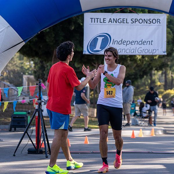Two runners high-fiving under an archway at the finish line. One in red, the other wearing a race bib.