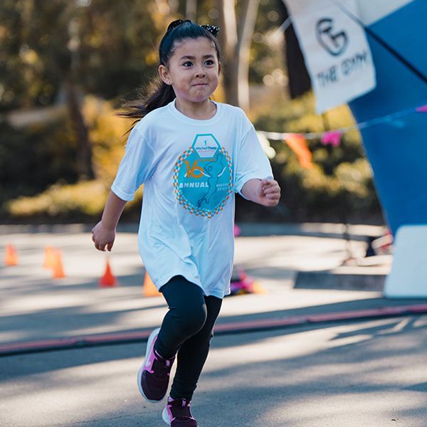 A young child running a race, wearing a white t-shirt and black leggings.