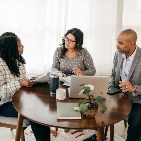 A group of people are sitting around a table with a laptop.