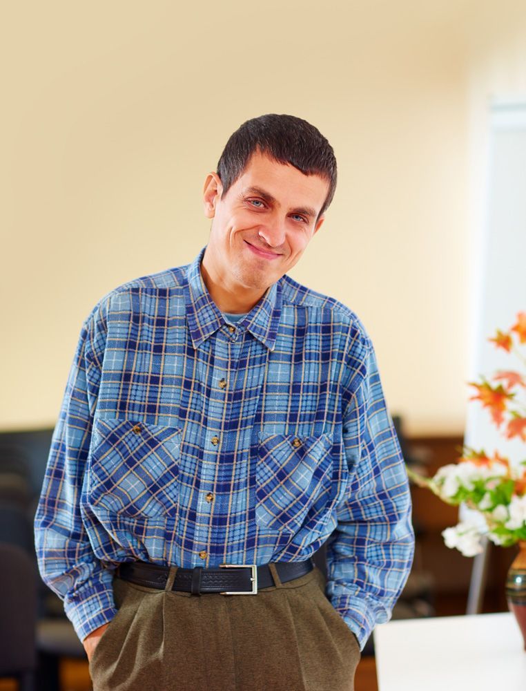 A man in a plaid shirt is smiling with his hands in his pockets