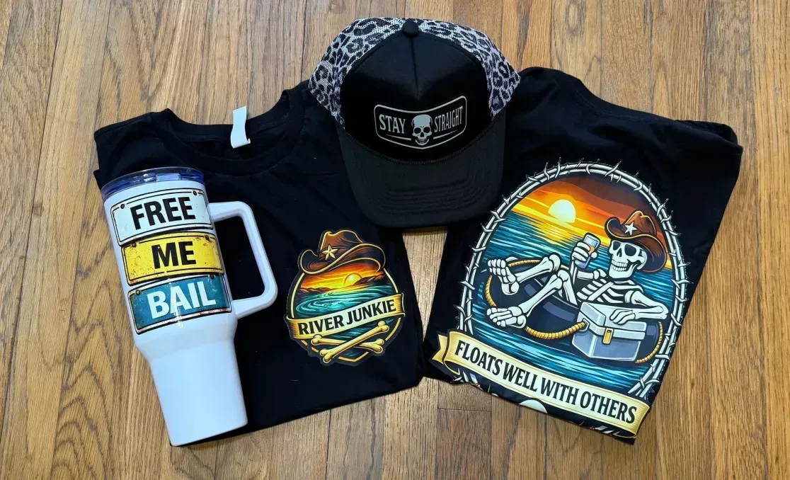 A black baseball cap, two black shirts with skeleton graphics, and a white tumbler saying 