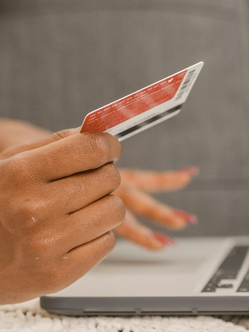A hand holding a red credit card near a laptop keyboard, representing online shopping or banking.