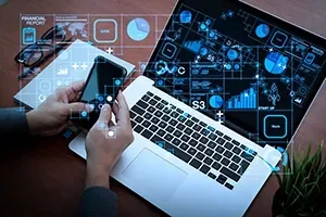 A person holds a smartphone over a laptop, with digital financial charts and data icons overlaid on the scene.
