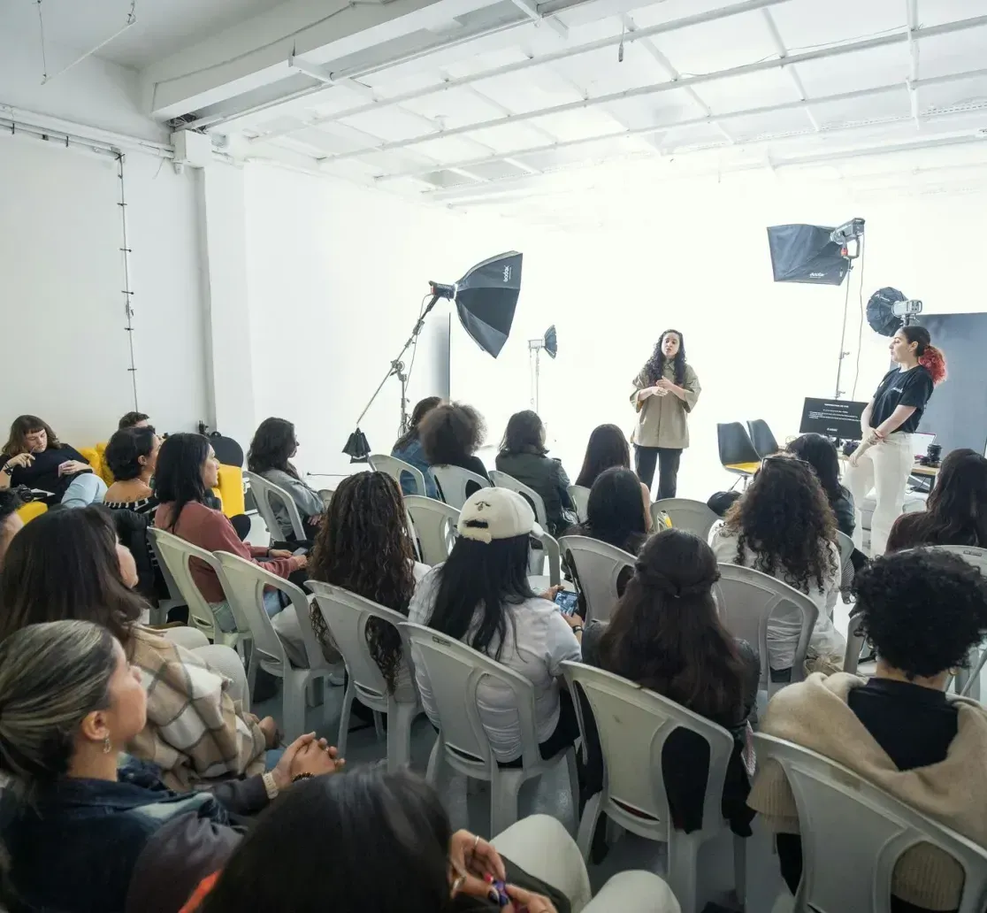 A presentation in a bright studio with a person speaking to a seated audience of attendees, with photography equipment.