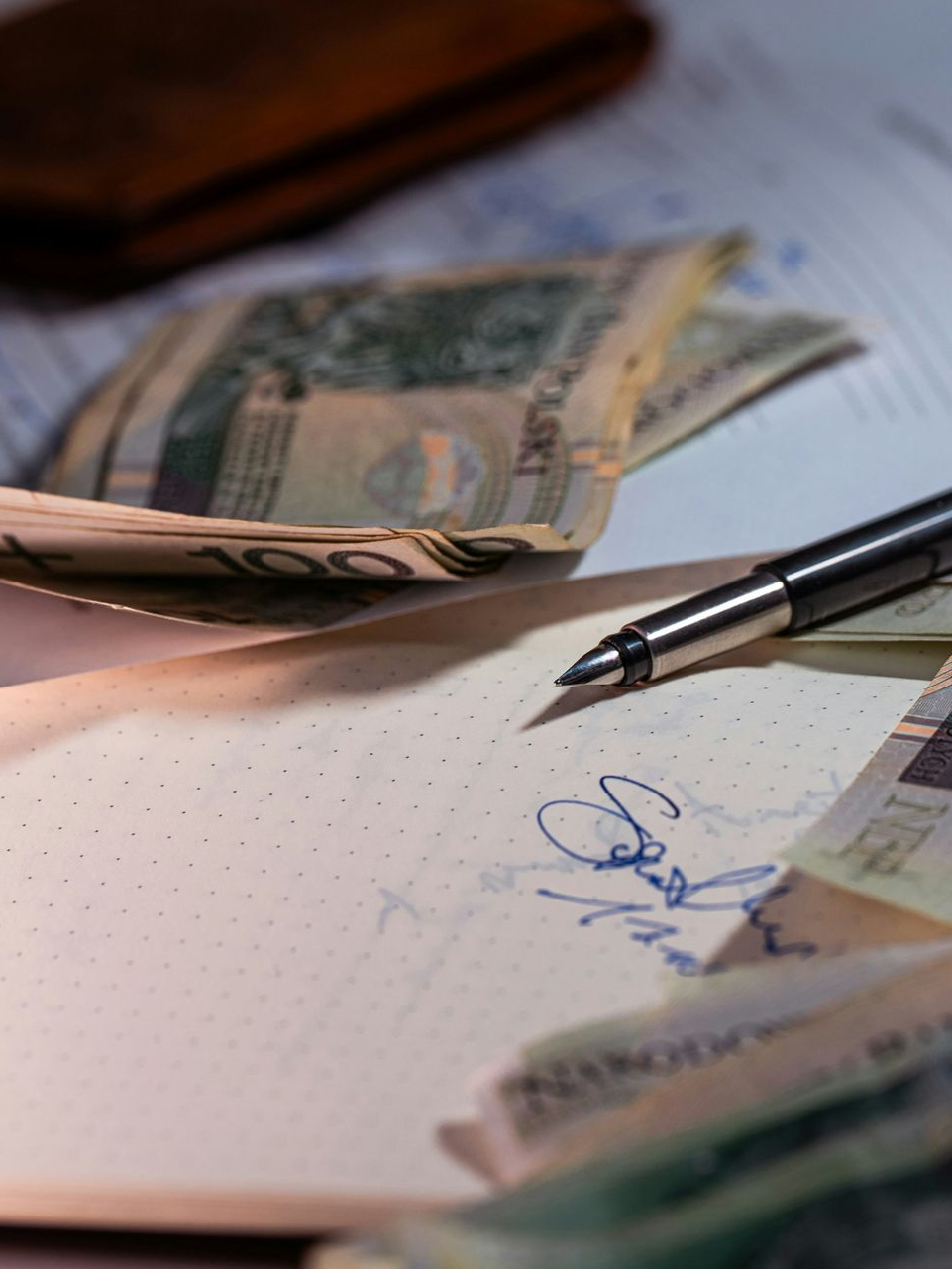 A black pen rests on a piece of paper with a signature next to stacks of Polish zloty banknotes.