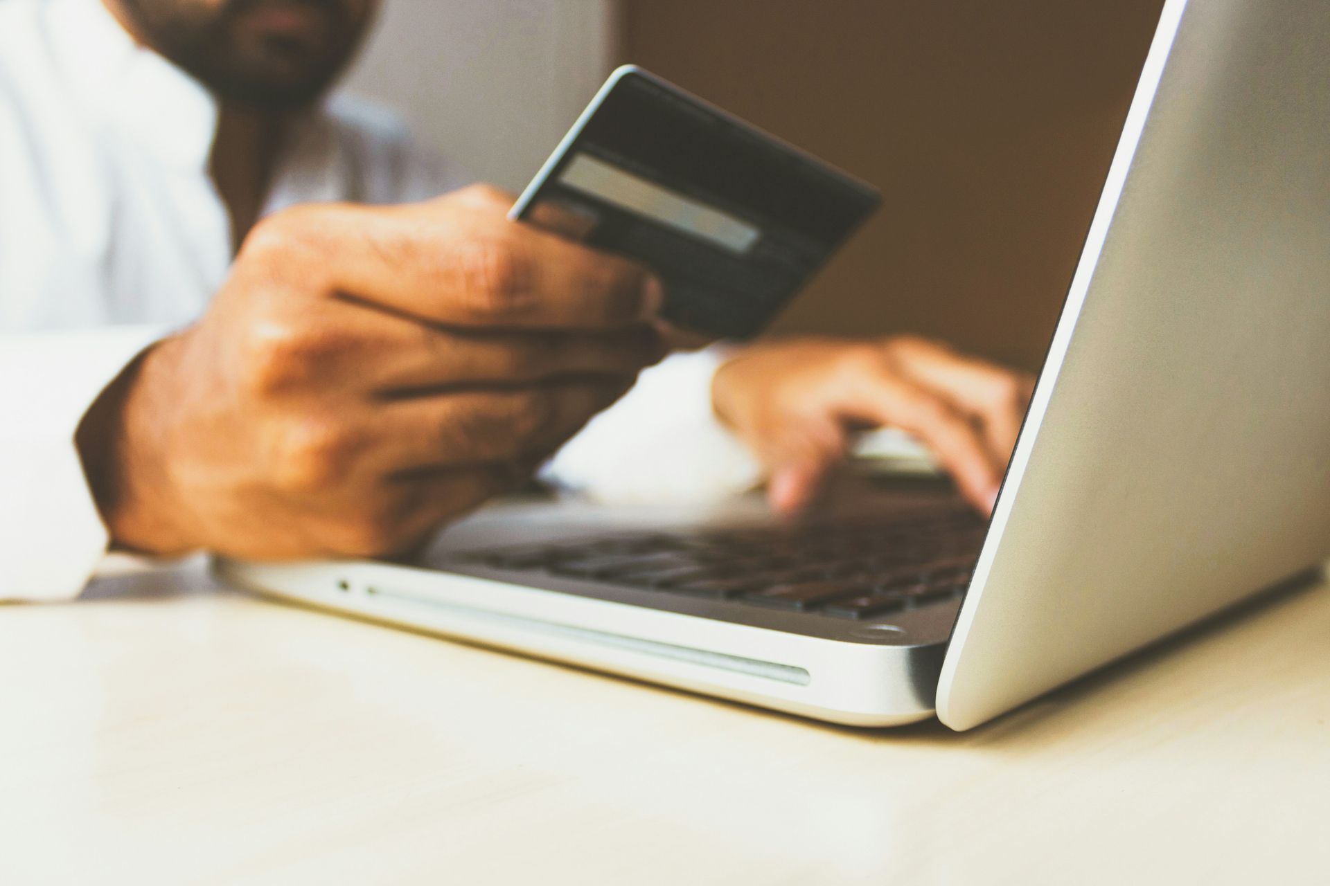 A person in a white shirt holding a credit card while typing on a laptop computer.