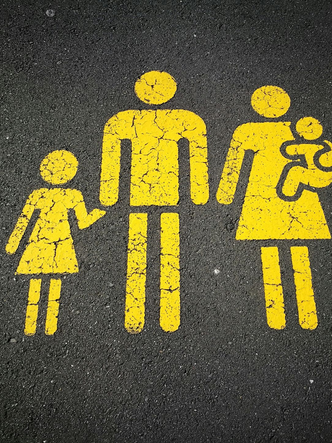 A yellow painted icon of a family of four on dark asphalt.