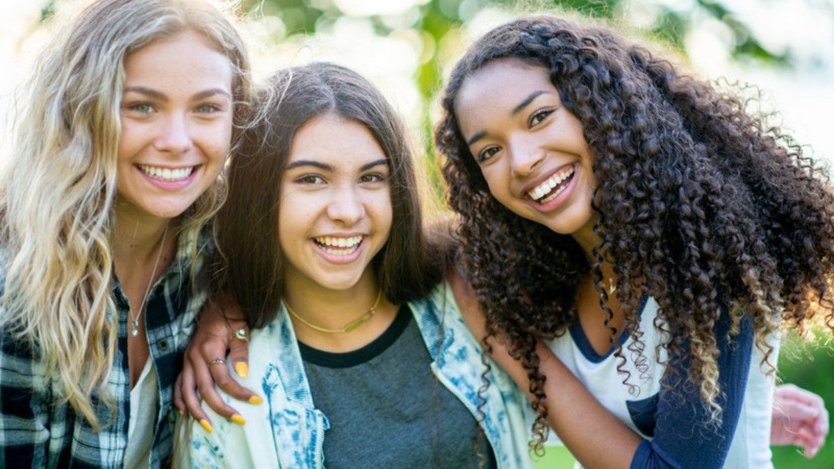 Three young women are posing for a picture together and smiling.