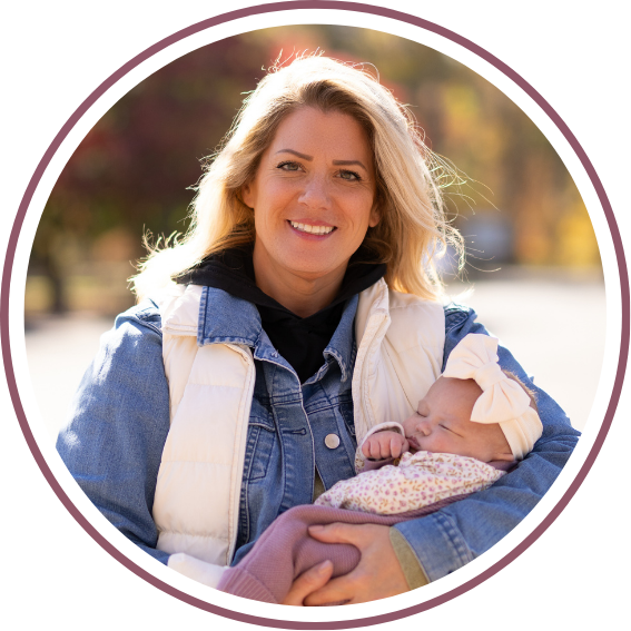 Woman in denim jacket holds sleeping baby outdoors.