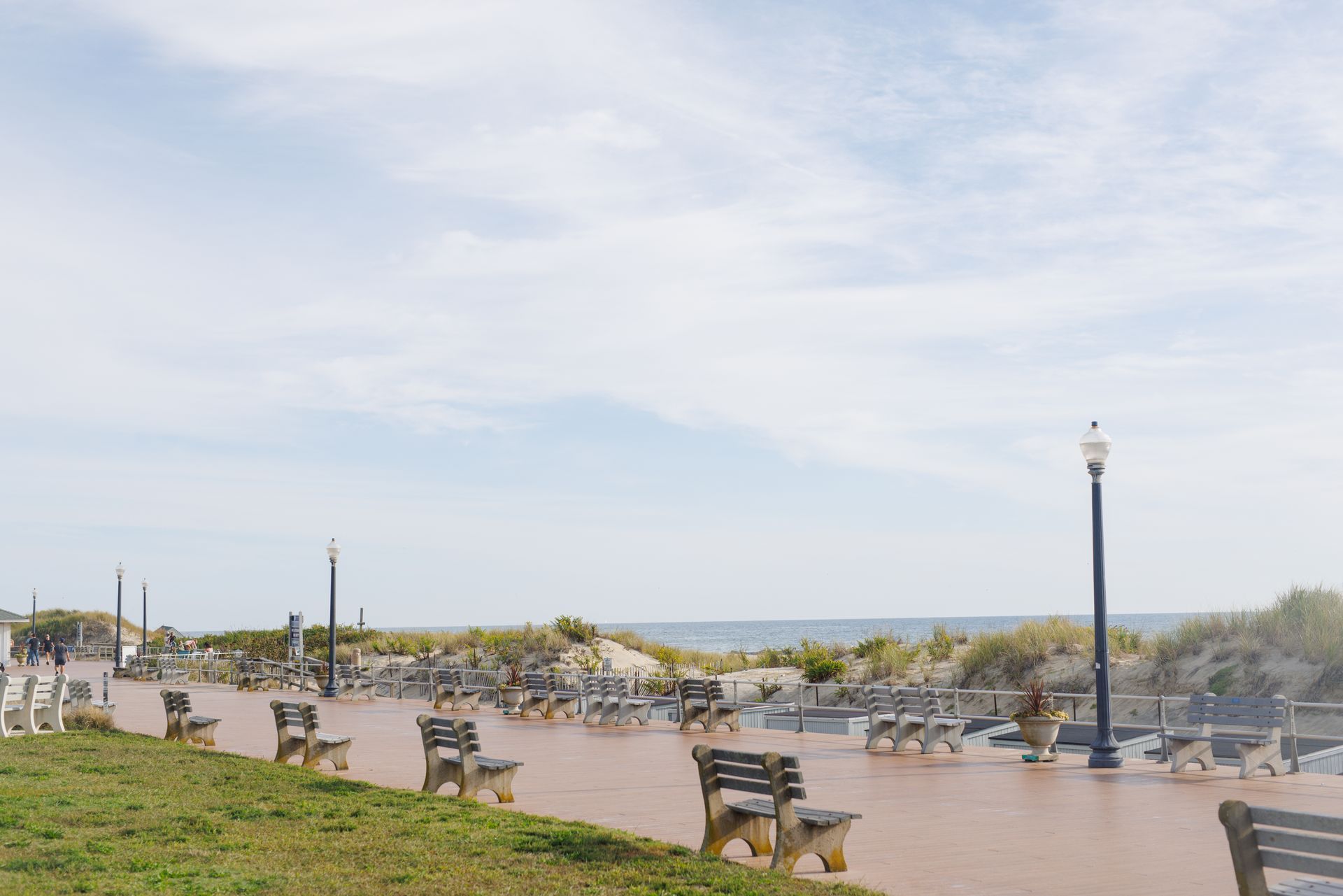 Pathway with benches, overlooking ocean and dunes under a blue sky.