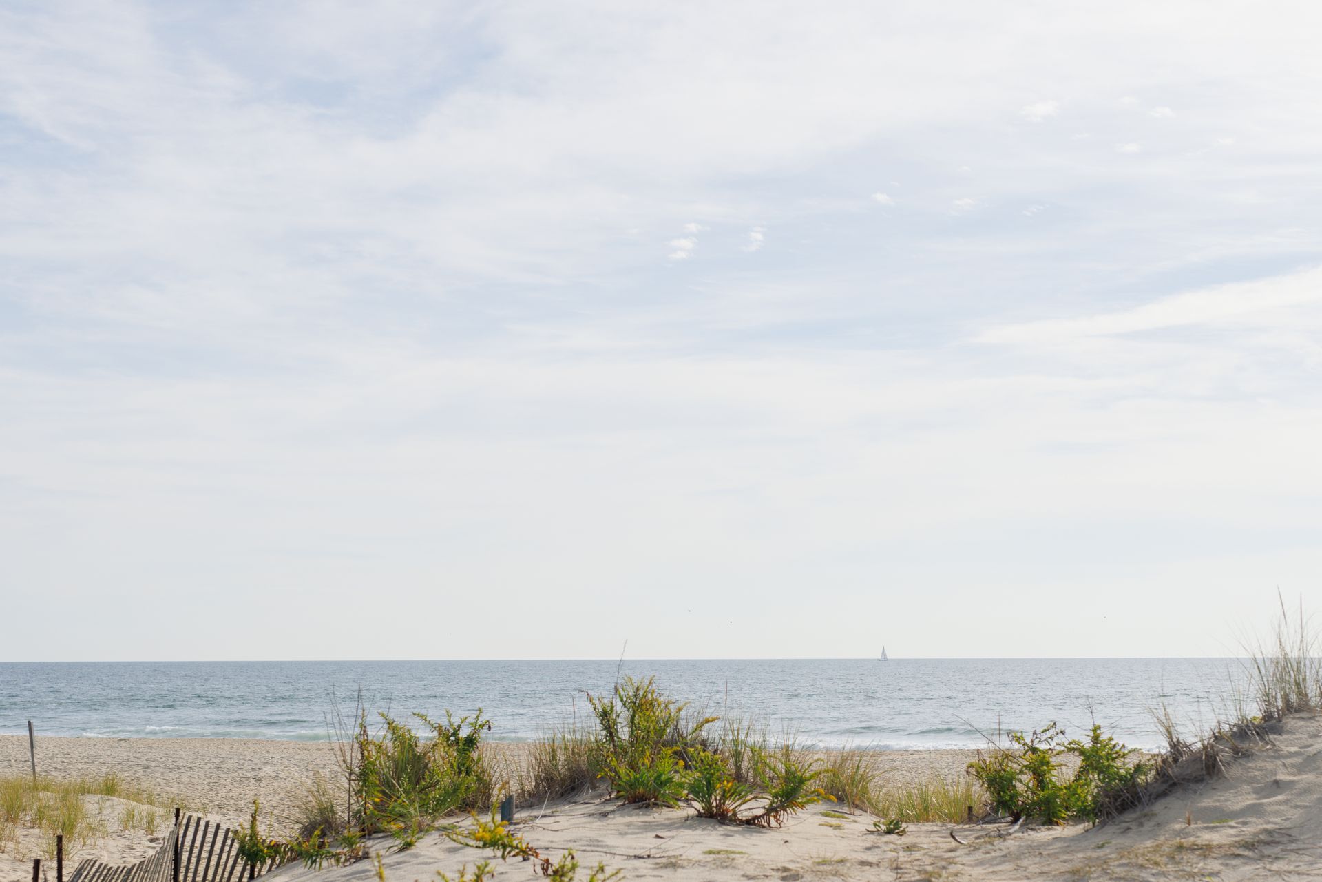 Beach scene with sand dunes, ocean, and cloudy sky.
