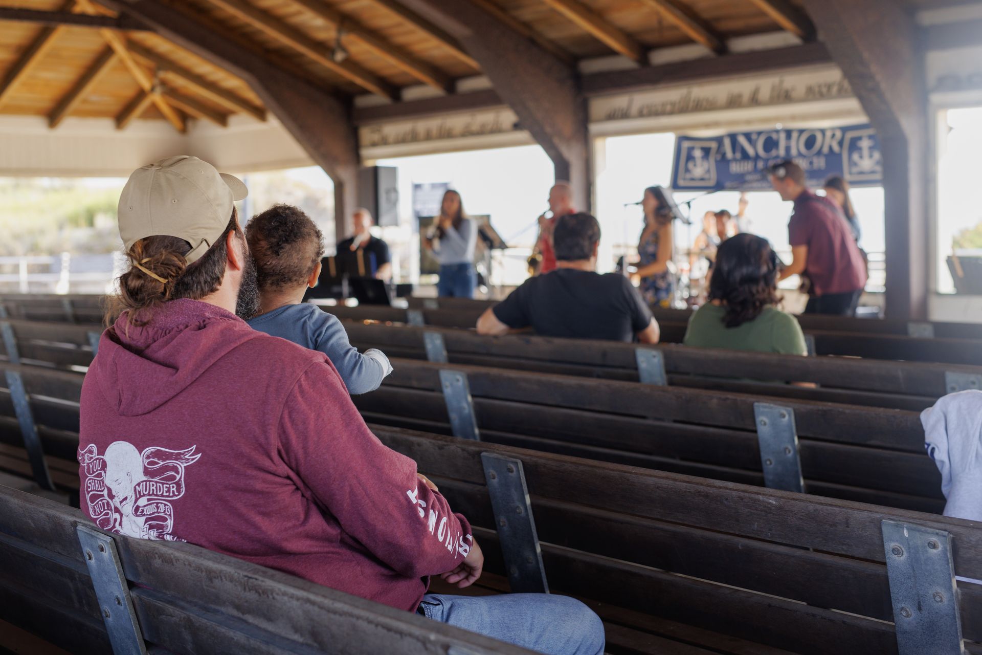 Man with child watching a band perform on stage in an outdoor pavilion.