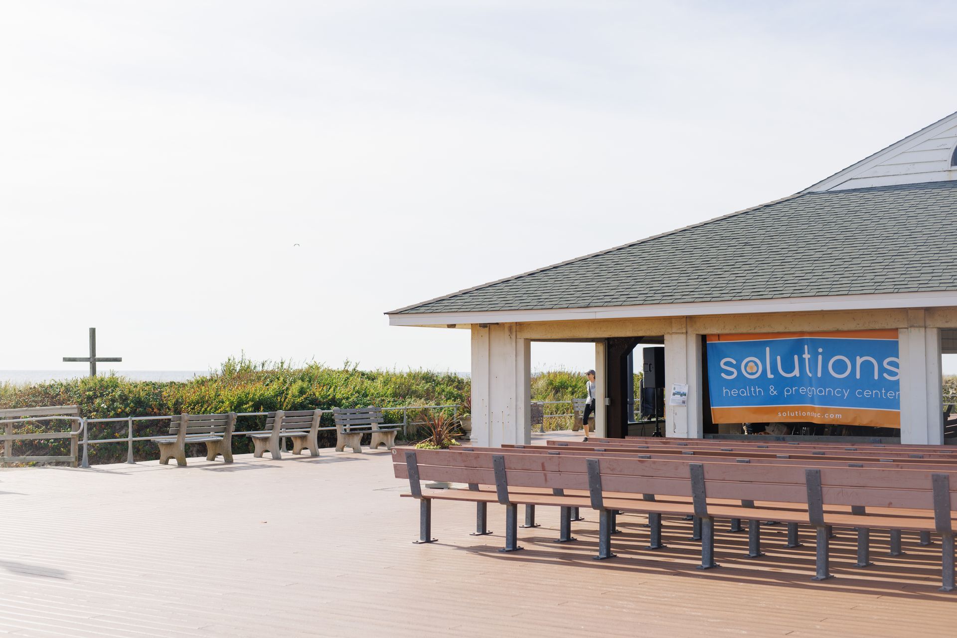 Beachfront structure with rows of benches, cross on the horizon.